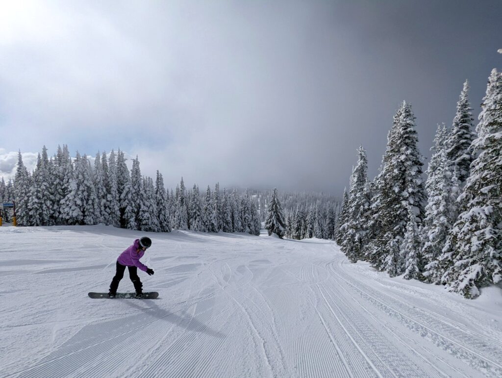 Back view of Gemma snowboarding down snow covered ski hill